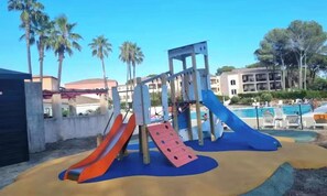 Ein Spielplatz mit Rutschen und Klettergerüsten, umgeben von Palmen und einem Schwimmbecken.