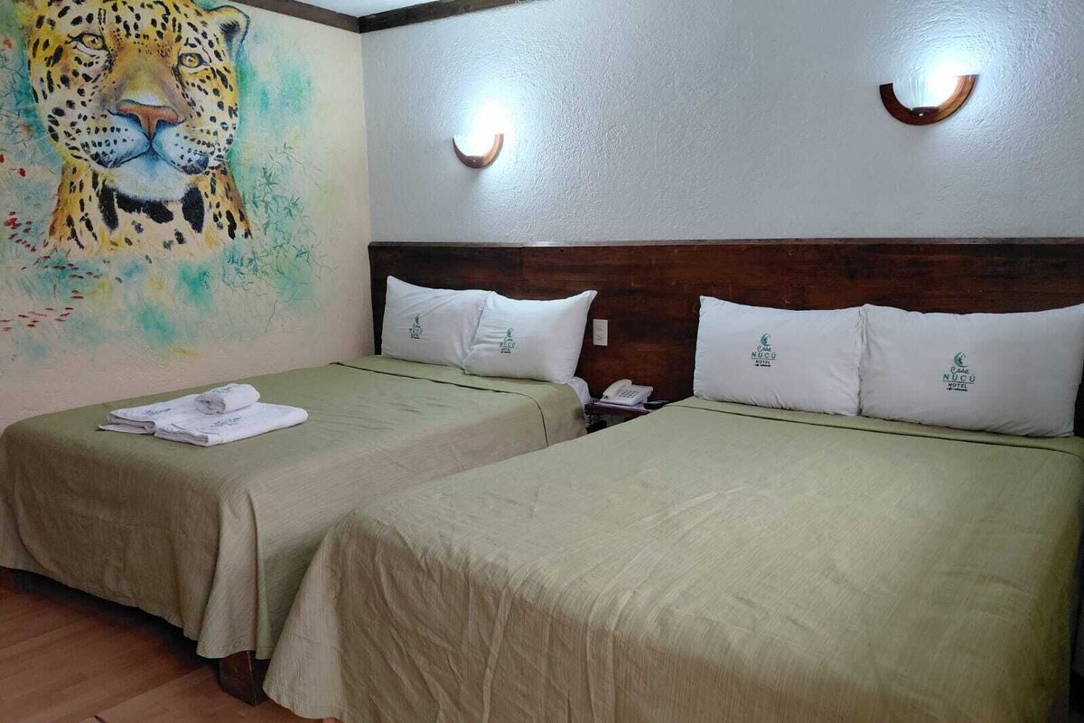 A hotel room with two beds, a painting of a leopard, and a wooden headboard.