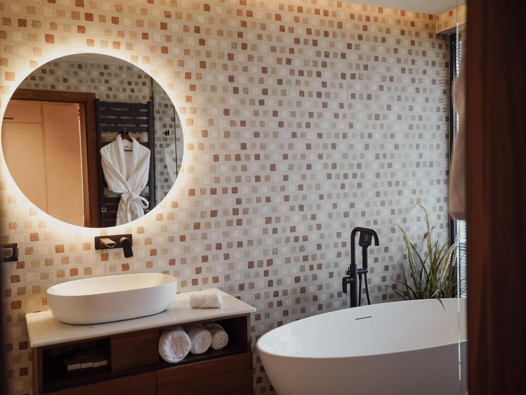 Ein Badezimmer mit rundem Spiegel, Waschbecken in Weiß, einer Badewanne und einer Wand mit Muster.