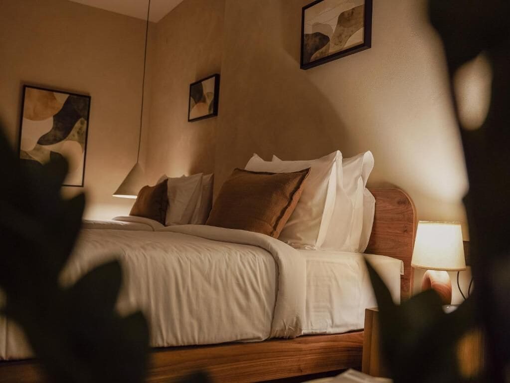 Une chambre à coucher avec un lit en bois, du linge de lit blanc et deux lampes fixées au mur.