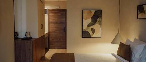 A hotel room with a bed, a desk, a chair, a lamp, and a painting on the wall.