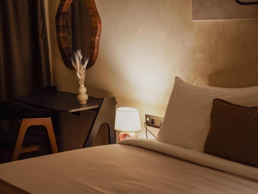 A hotel room with a bed, a desk, a lamp, and a wall-mounted mirror.