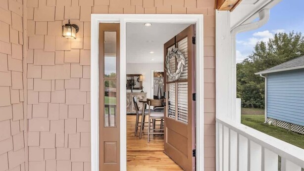 Une porte en bois donne accès à un espace intérieur comprenant un coin repas et offrant une vue sur l’extérieur.