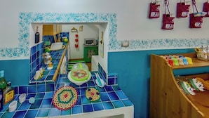 A kitchen with blue and white tiles, a sink, a microwave, and a wooden shelf with jars. - Casa Sarda (Sennori)