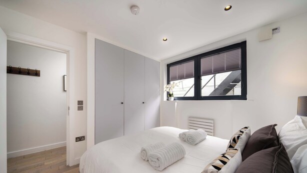 Un dormitorio con cama, toallas blancas, una ventana con persianas y una puerta con perchero.
