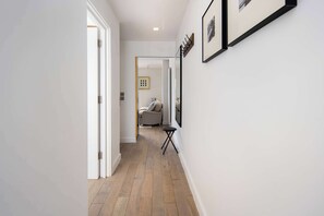 A hallway with a wooden floor, white walls, and a door leading to a room with a gray sofa and a small black table. - 1 Min Walk to Euston Station, Modern Apartment (Greater London)