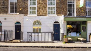 Un edificio con un letrero verde que dice 'The Sandwich Club', una puerta negra y un pequeño espacio de asientos al aire libre.