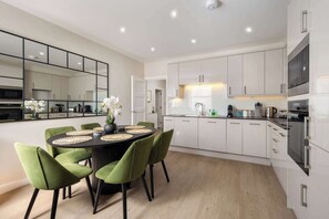 A modern kitchen with white cabinets, a dining area with green chairs, and a round table. - 10 Mins Walk to Bond Street, Marylebone Retreat (London)