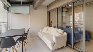Ein modernes Zimmer mit einer Couch, einem Tisch mit Stühlen und einer Glasschiebetür, die auf einen Balkon führt.