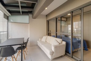 Ein modernes Zimmer mit einer Couch, einem Tisch mit Stühlen und einer Glasschiebetür, die auf einen Balkon führt.