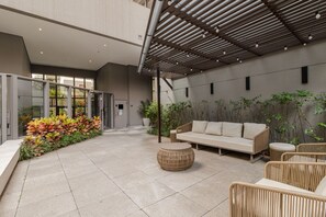 Ein moderner Außenbereich mit Sitzgelegenheiten, inklusive einer Couch und Korbstühlen, umgeben von Topfpflanzen und einer Pergola.