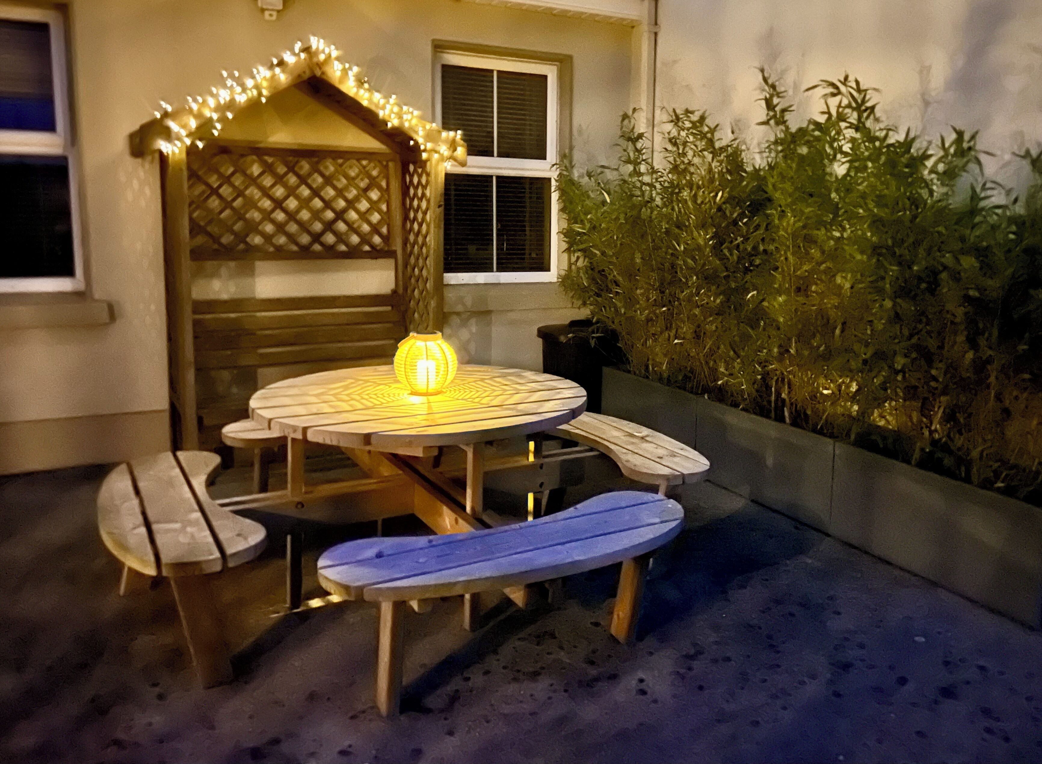 An outdoor seating area with a round table, benches, and a decorative light fixture.