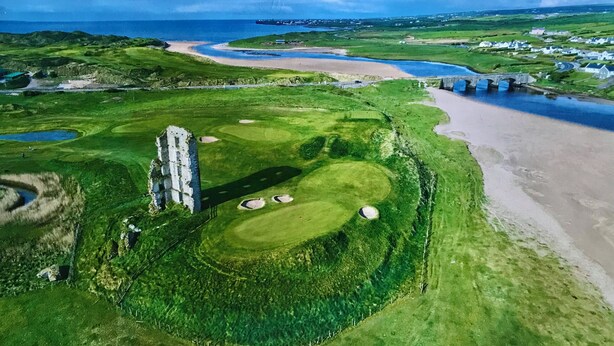 An aerial view of a golf course with bunkers, a bridge, and a beach.