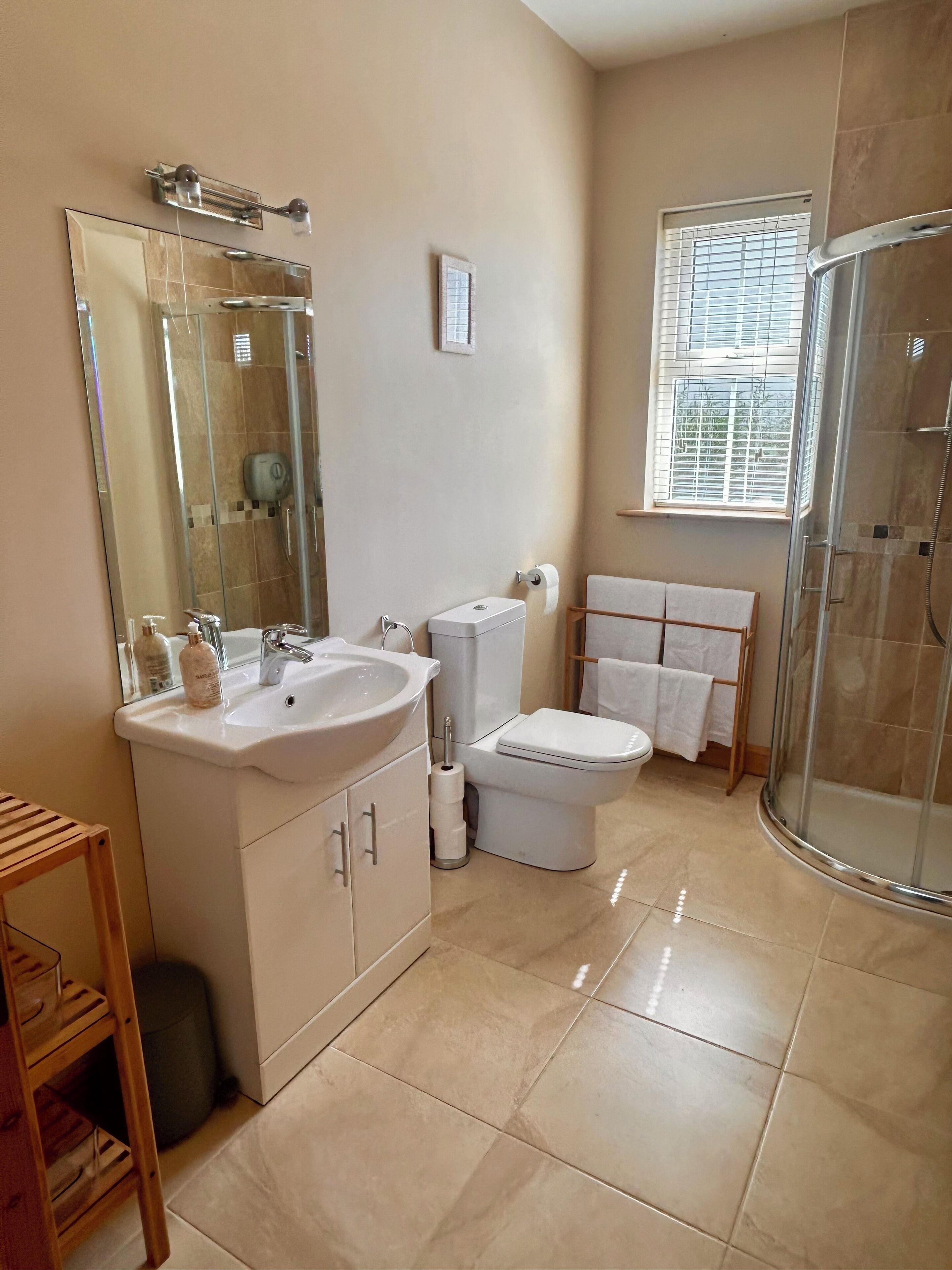Une salle de bain avec une douche à parois de verre, un lavabo avec un miroir, des toilettes et une fenêtre avec des stores.