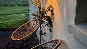A wicker chair outside a building with a wall-mounted lamp and a view of the landscape.