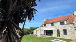Une maison en pierre avec un toit recouvert de tuiles rouges, une cour verdoyante et une terrasse en bois.