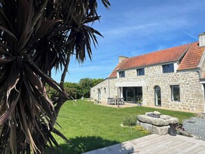 A stone house with a red-tiled roof, a grassy yard, and a wooden deck. - Breton house with footpath to coast in Finistère (Plouescat)
