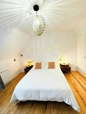 A bedroom with a large bed, a hanging light fixture, bedside tables with lamps, and a radiator. - Breton house with footpath to coast in Finistère (Plouescat)
