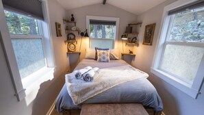 Quarto com cama, mesas de cabeceira, um banco e janelas.