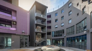 Ein modernes Gebäude mit mehreren Etagen, Balkonen und einem zentralen Innenhof mit einer Sitzgruppe in Kreisform.