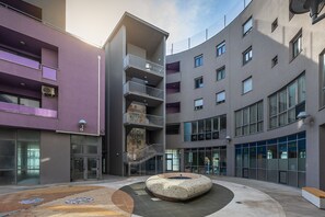 Ein modernes Gebäude mit mehreren Etagen, Balkonen und einem zentralen Innenhof mit einer Sitzgruppe in Kreisform.