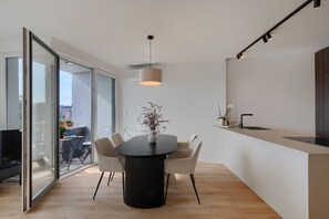 Eine moderne Küche mit einem runden Esstisch, Stühlen, einer Pendelleuchte und Blick durch eine Glastür.