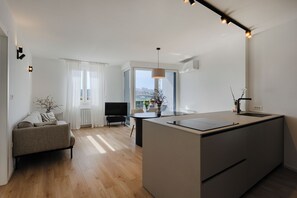 Eine moderne Wohnung mit Kücheninsel, Sofa, Fernseher und Blick auf die Stadt.