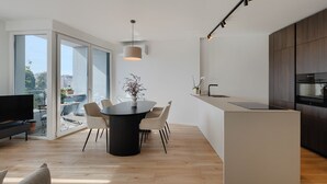 Eine moderne Küche mit Einbauofen, einem Essbereich mit rundem Tisch und Stühlen sowie einer großen Schiebeglastür, die auf einen Balkon führt.