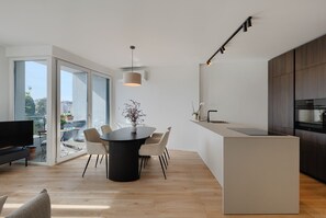 Eine moderne Küche mit Einbauofen, einem Essbereich mit rundem Tisch und Stühlen sowie einer großen Schiebeglastür, die auf einen Balkon führt.