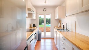 Cocina estrecha con armarios blancos, encimera de madera y vista a un espacio exterior a través de la puerta de cristal.