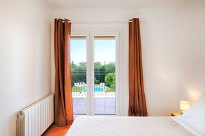 Ein Schlafzimmer mit Bett, Nachttisch, Lampe und Blick auf ein Schwimmbecken durch eine Glasschiebetür.