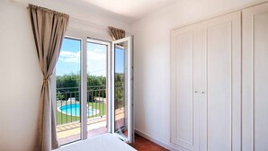 Un dormitorio con una cama grande, un ventanal corredero a un balcón y un armario blanco.