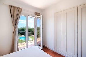 Ein Schlafzimmer mit einem großen Bett, einer Schiebetür zum Balkon und einem weißen Kleiderschrank.