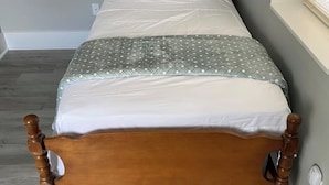 Un lit simple avec une tête de lit en bois, une couvre-lit à motifs et un mur uni avec une fenêtre.