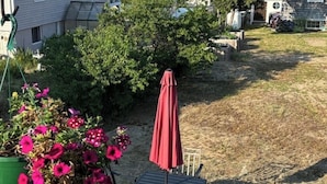 Une terrasse avec une table et des chaises, un parasol rouge et un pot de fleurs orné de fleurs roses.