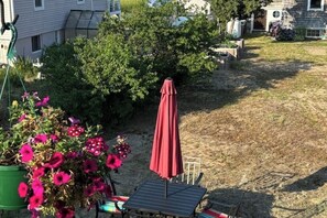 Eine Terrasse mit Tisch und Stühlen, einem roten Sonnenschirm und einem Blumentopf mit rosa Blüten.