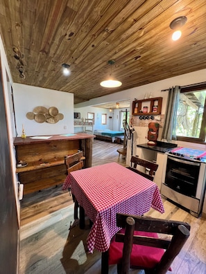 A rustic kitchen with a wooden ceiling, a dining table with a checkered tablecloth, and a kitchenette with a stove. - Exclusive chalet with sea and mountain views, just meters from the beach. (Paraty)