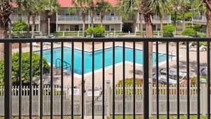 A pool with a red-roofed building in the background, surrounded by palm trees and a white fence. -  1-bedroom condo in gorgeous Sea grove beach , pool and 5 min walk to the beach (Santa Rosa Beach)