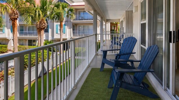 A balcony with two blue Adirondack chairs, a white railing, and a green artificial turf. -  1-bedroom condo in gorgeous Sea grove beach , pool and 5 min walk to the beach (Santa Rosa Beach)