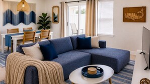 A living room with a sectional sofa, a coffee table, a ceiling fan, a dining area with a table and chairs, and a large window with curtains. -  1-bedroom condo in gorgeous Sea grove beach , pool and 5 min walk to the beach (Santa Rosa Beach)