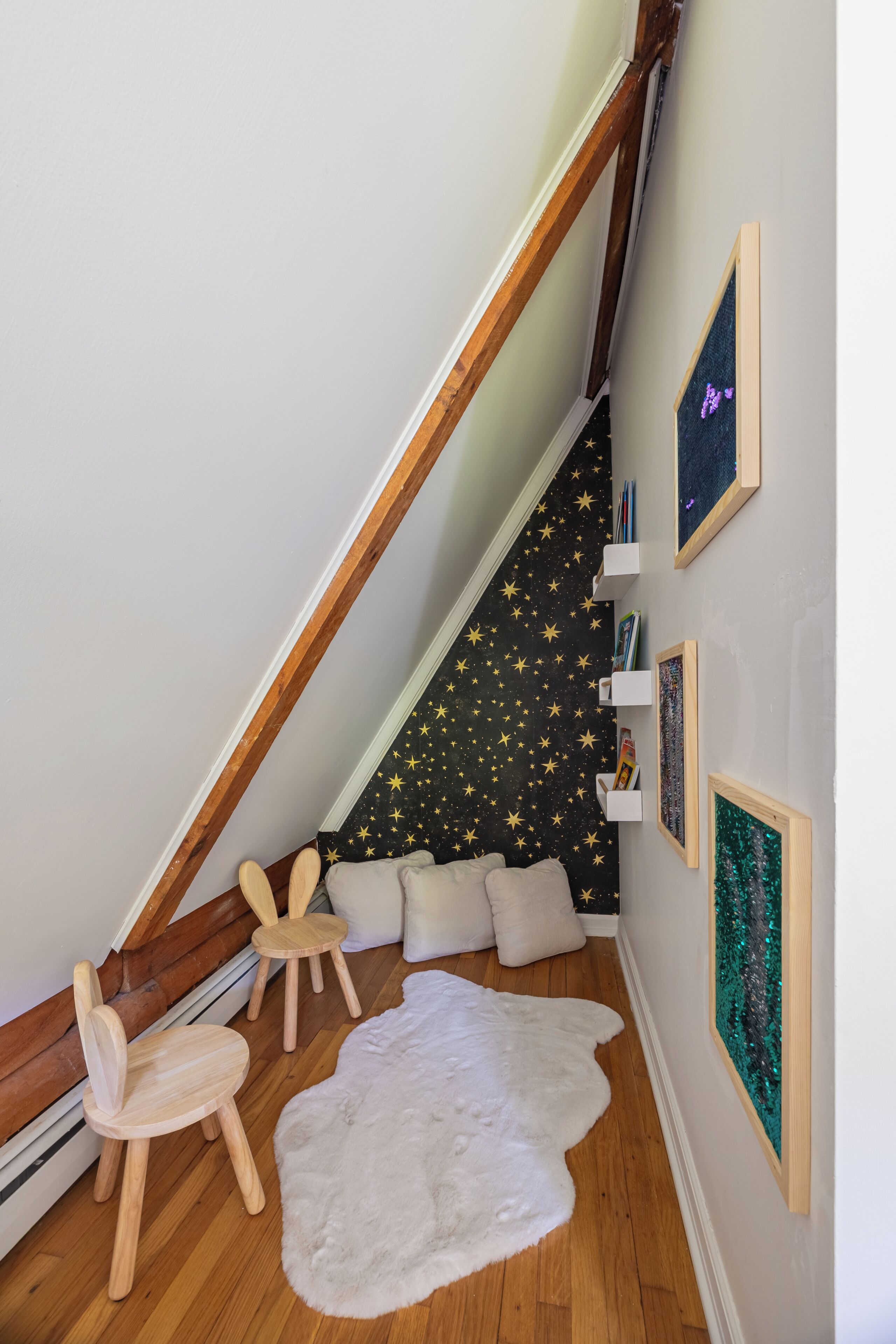 A cozy room with a sloped ceiling, wooden chairs, a white furry rug, star-patterned wall, and framed pictures.