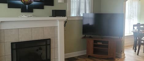 Ein Wohnzimmer mit Kamin, Flachbildfernseher, Deckenventilator und einem gemusterten Teppich.