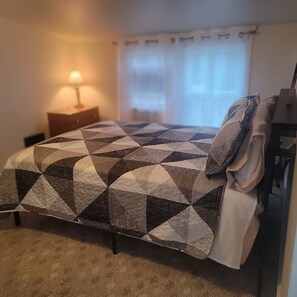 Ein Schlafzimmer mit einem Bett, einem Nachttisch, einer Lampe und einem Fenster mit Vorhängen.