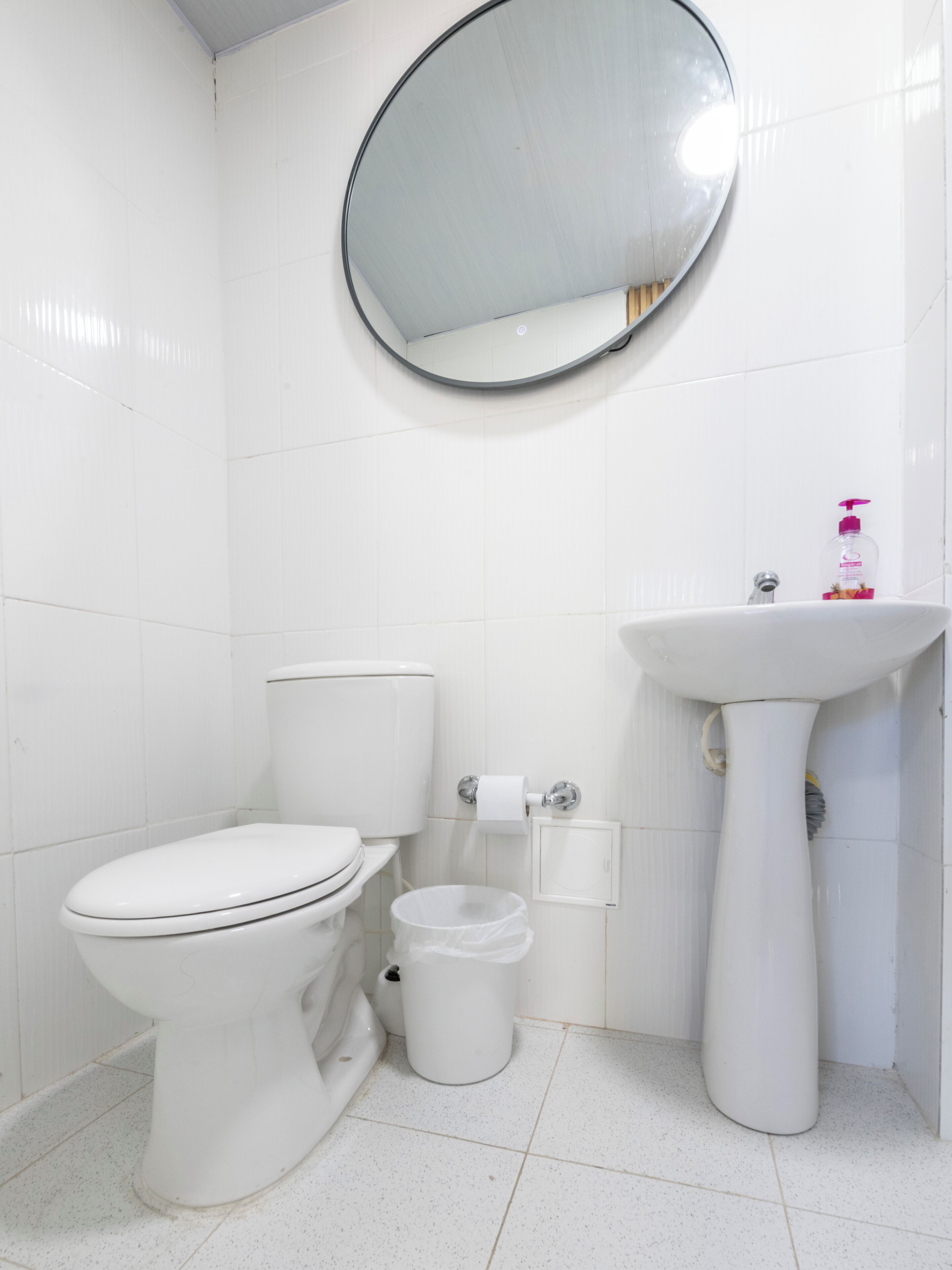 A bathroom with a toilet, bidet, sink, and a round mirror on the wall.