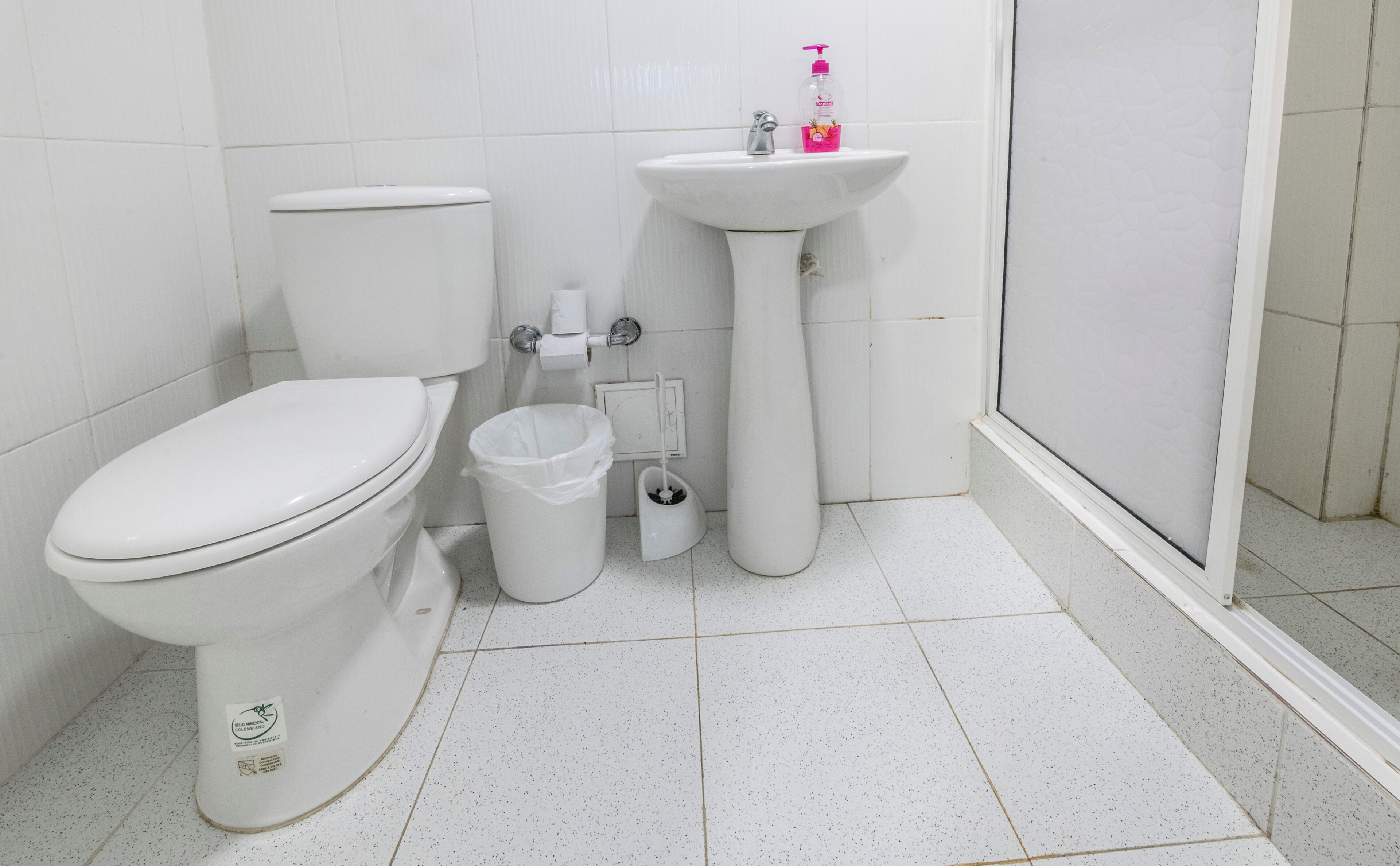 A bathroom with a toilet, a sink, a trash bin, and a shower area.