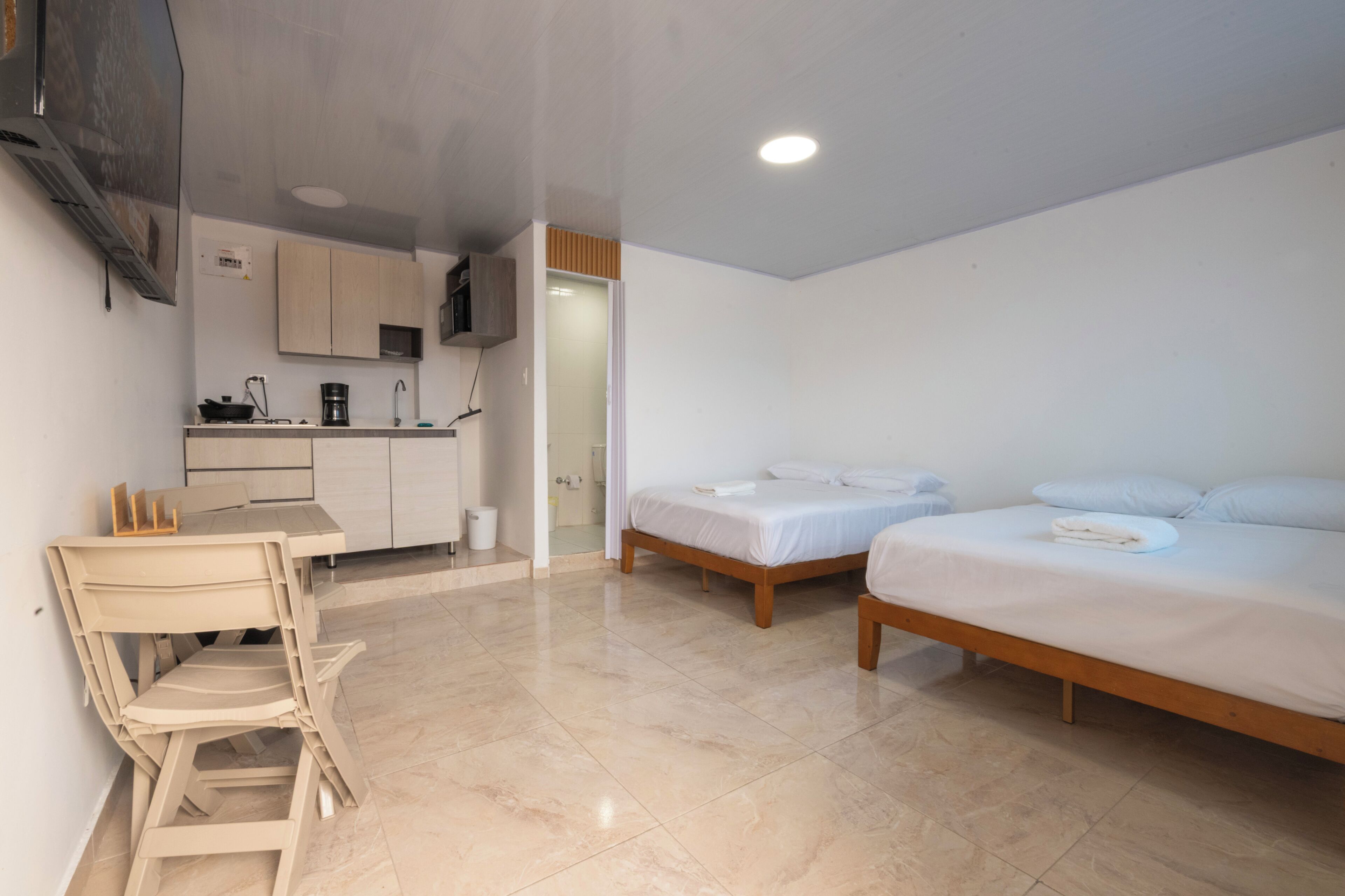 Habitación de hotel moderna con kitchenette, dos camas individuales, zona de comedor con sillas y baño.