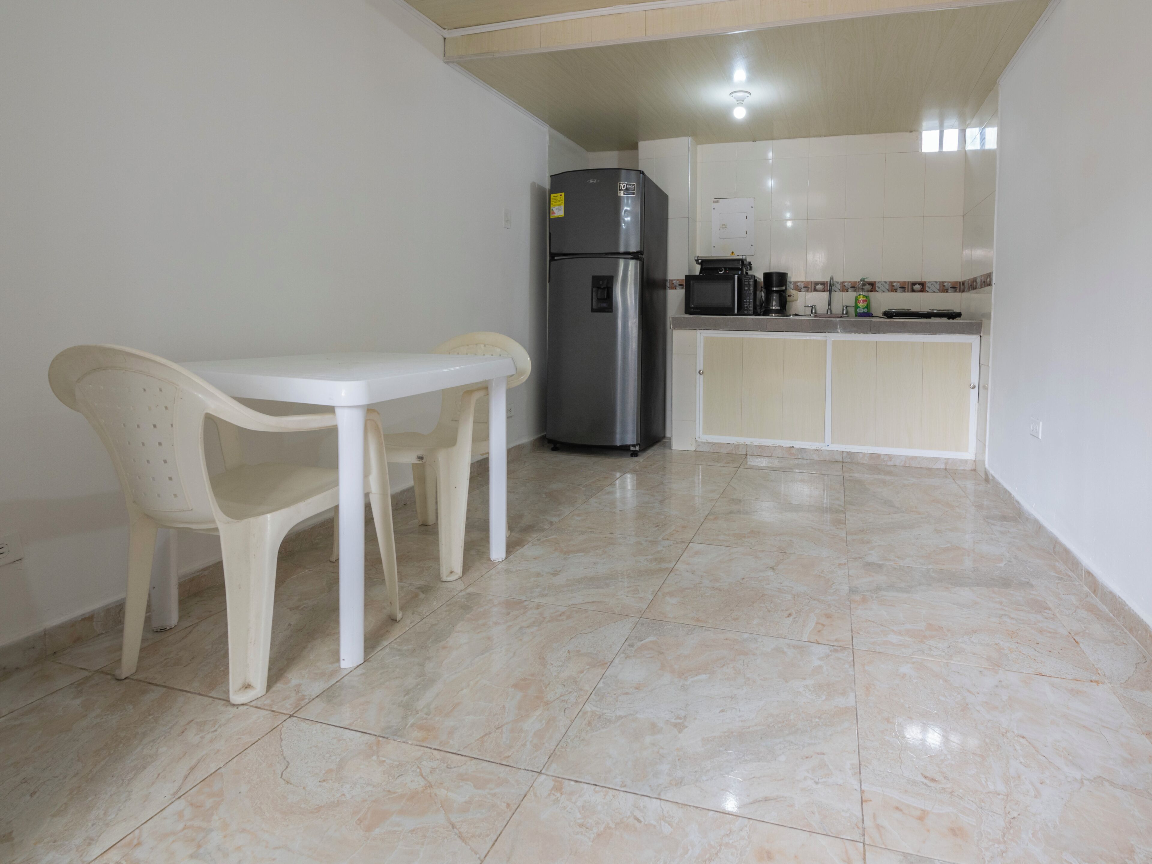 A kitchen with a white table, two chairs, a refrigerator, and a microwave.