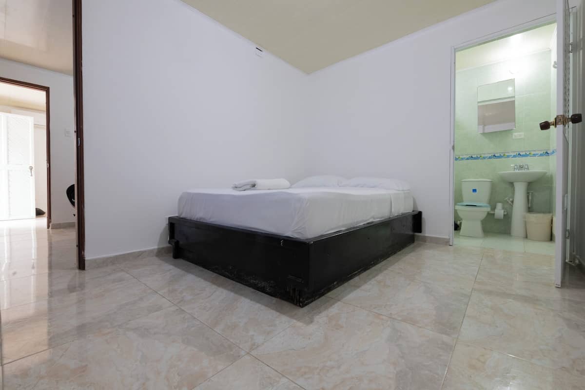 A bedroom with a bed, a bathroom with a toilet and sink, and a door leading to another room.