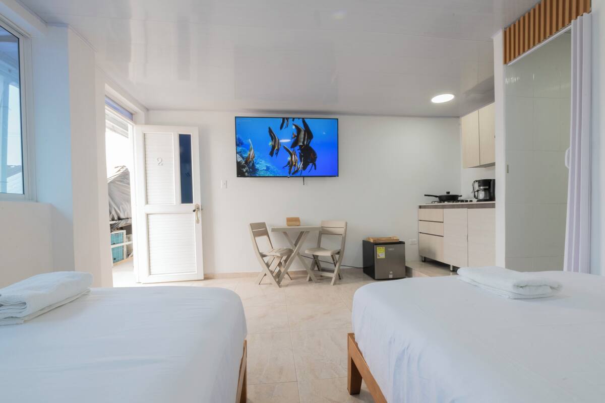 A hotel room with two beds, a desk, a chair, a TV, and a kitchenette.