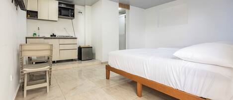A bedroom with a bed, a small desk, a microwave, and a cabinet.